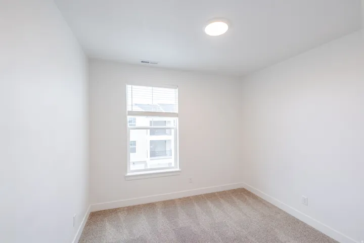 Neutral tone wall finish, textured carpet flooring, window with blinds, recessed ceiling light, and white baseboards