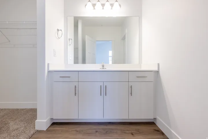 Bathroom vanity featuring light-toned cabinetry with brushed nickel hardware, a white countertop, and an integrated rectangular sink with a chrome faucet