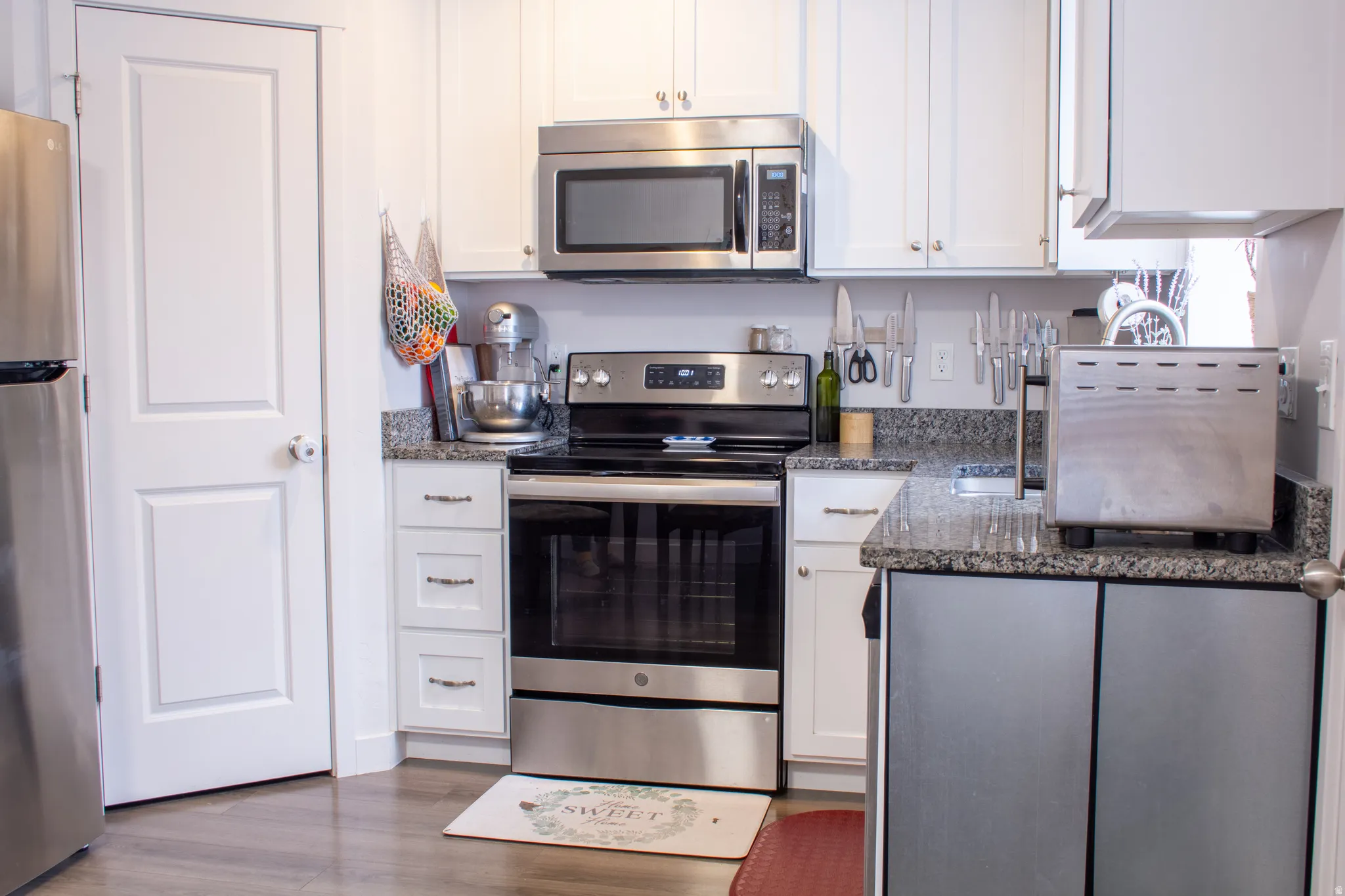 Kitchen with appliances with stainless steel finishes, white cabinets, dark stone countertops, and wood finished floors