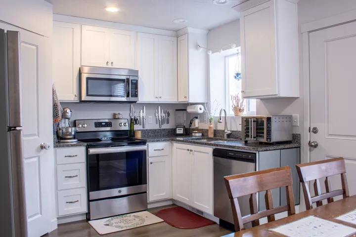 Kitchen with stainless steel appliances, white cabinets, dark wood-style flooring, dark stone counters, and recessed lighting
