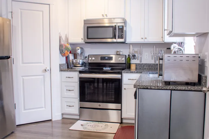 Kitchen with appliances with stainless steel finishes, white cabinets, dark stone countertops, and wood finished floors