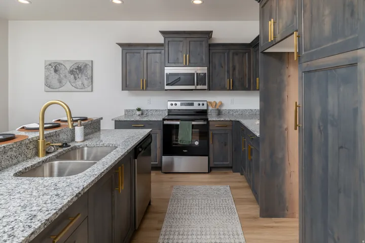 Kitchen featuring light wood-finish flooring, granite countertops, stainless steel appliances, and dark wood cabinetry with gold-tone hardware