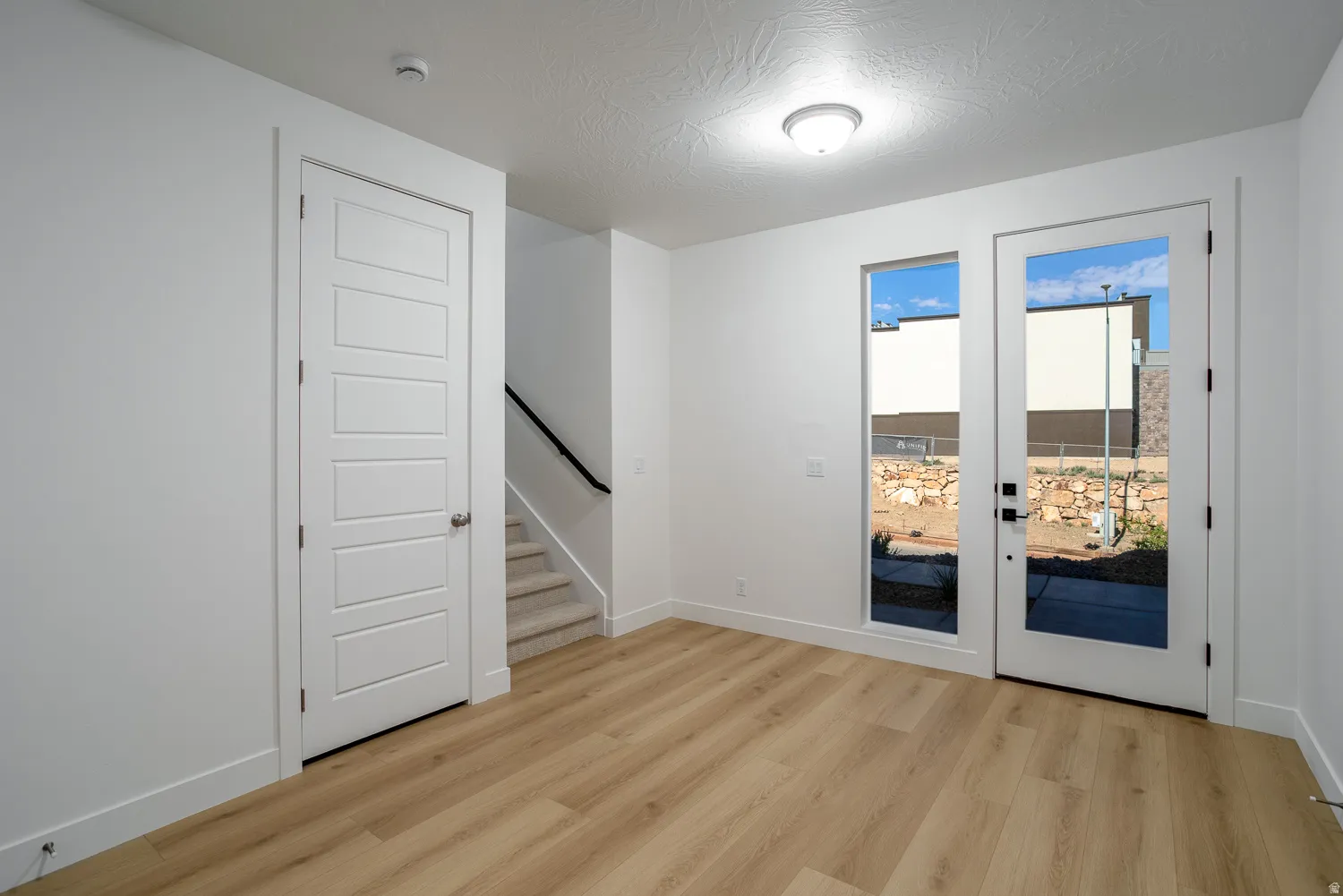 Empty room featuring stairs, light wood-type flooring, a textured ceiling, and french doors
