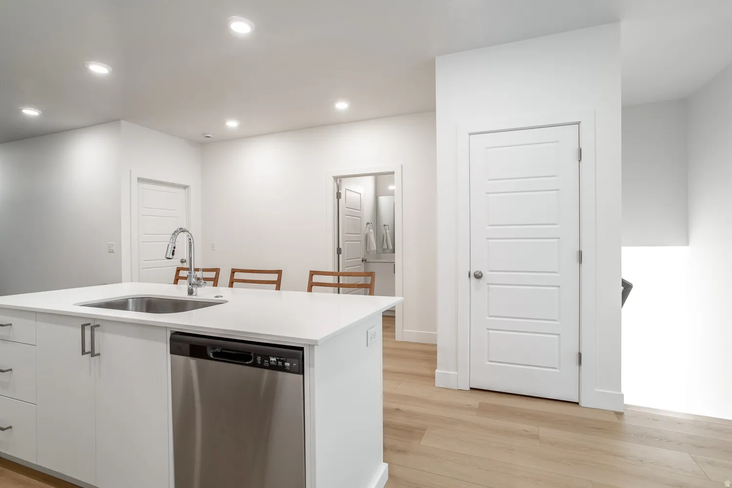 Kitchen featuring white cabinets, dishwasher, recessed lighting, light wood-style floors, and a kitchen breakfast bar