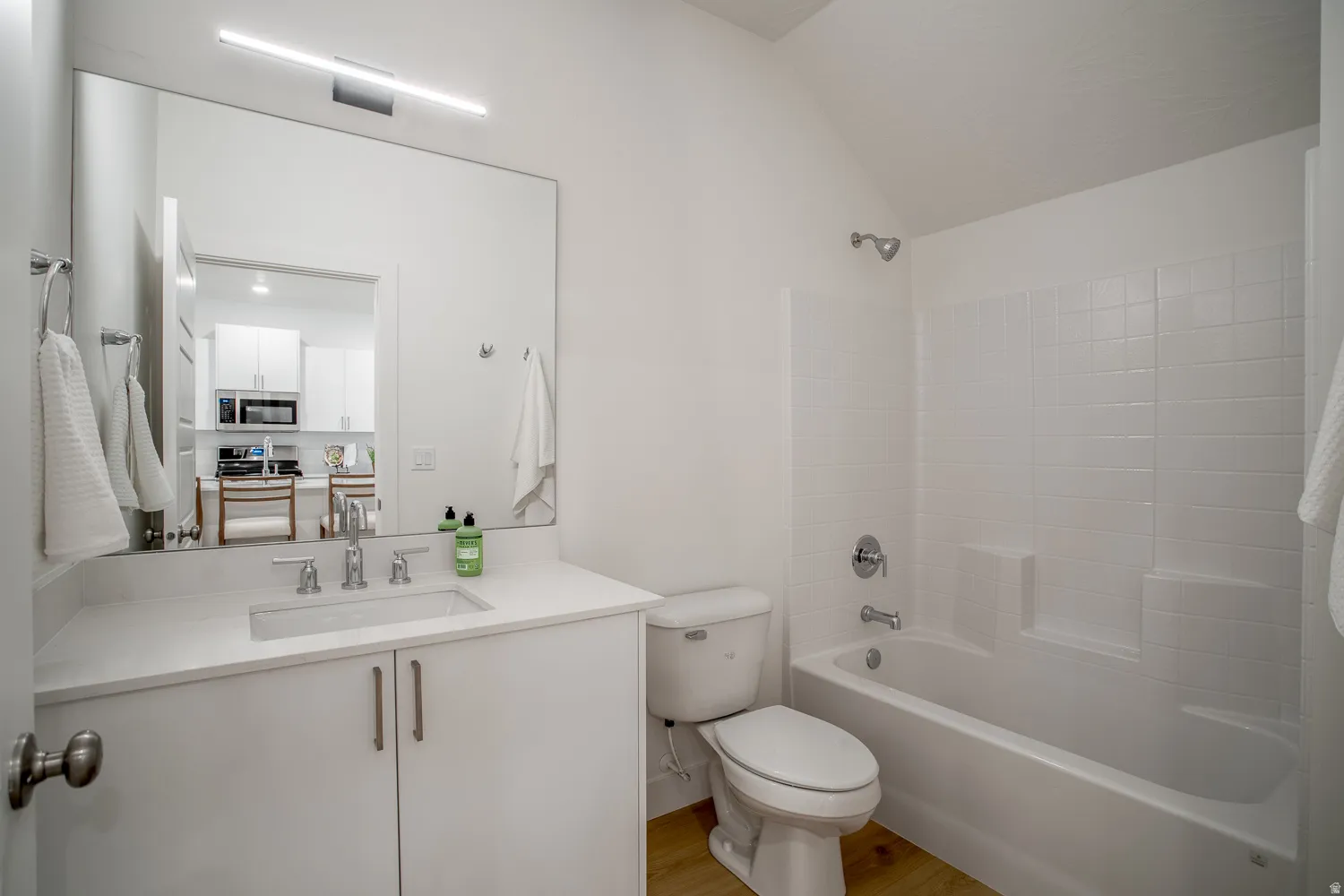 Full bathroom with shower / bath combination, vanity, light wood-style flooring, and vaulted ceiling