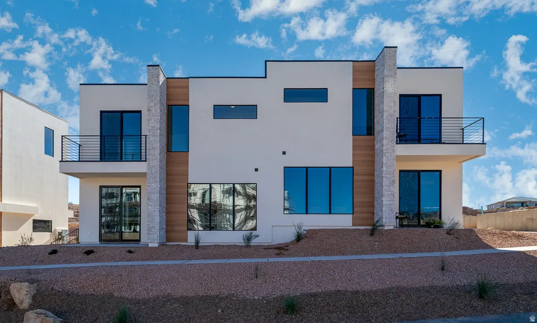 Rear view of house featuring a balcony, stucco siding, and stone siding
