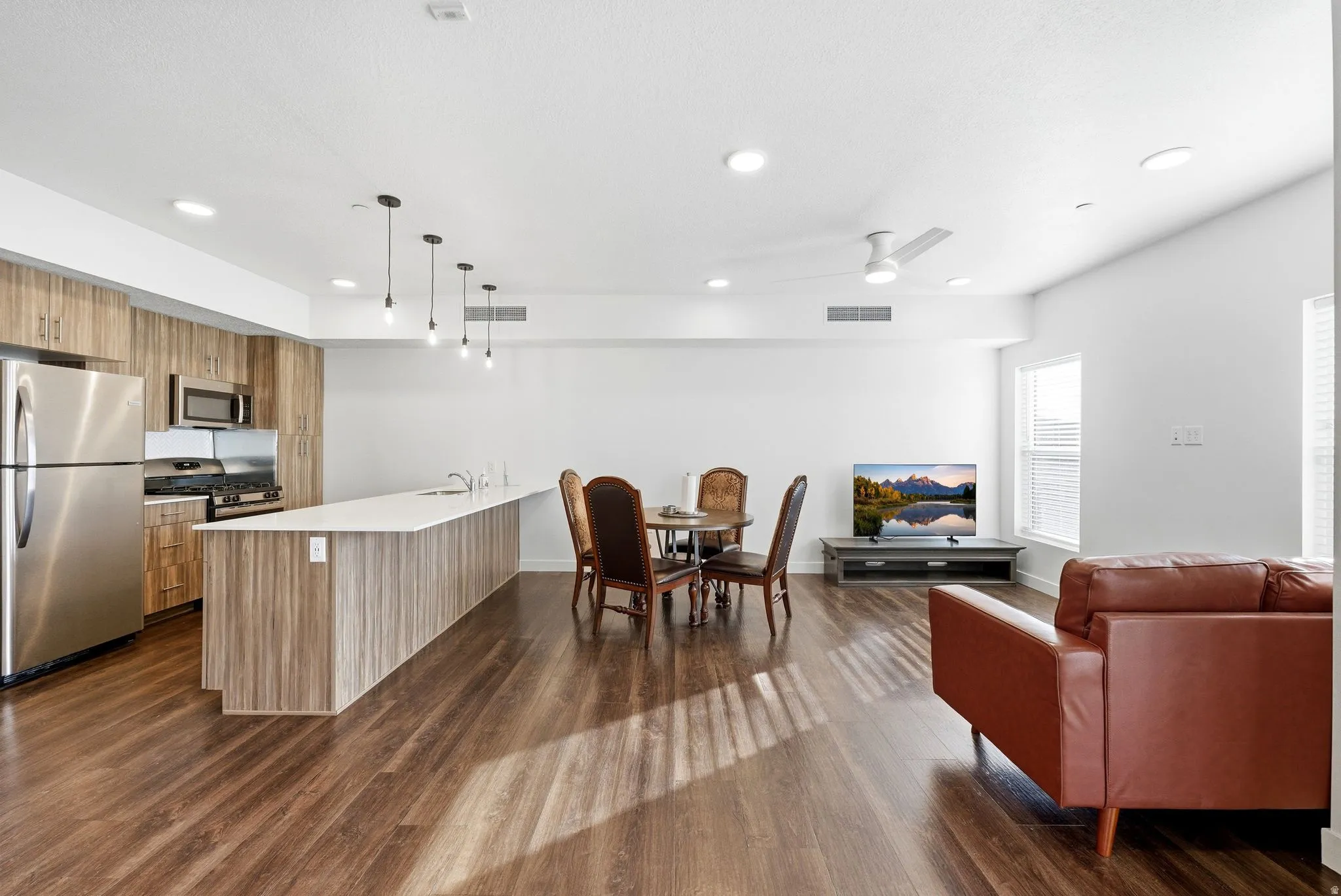 Kitchen featuring open floor plan, stainless steel appliances, modern cabinets, decorative light fixtures, and a kitchen breakfast bar