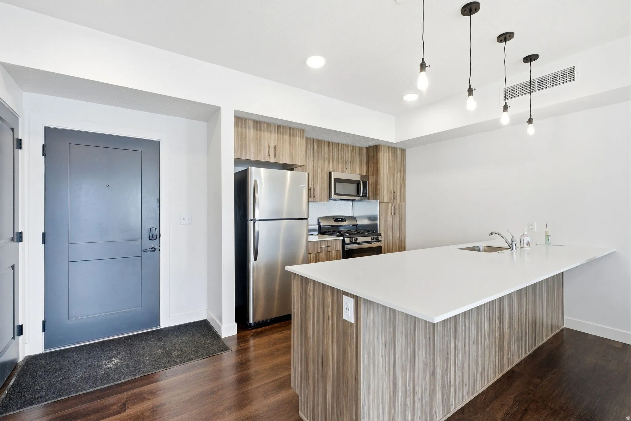 Kitchen featuring brown cabinets, appliances with stainless steel finishes, pendant lighting, a peninsula, and modern cabinets