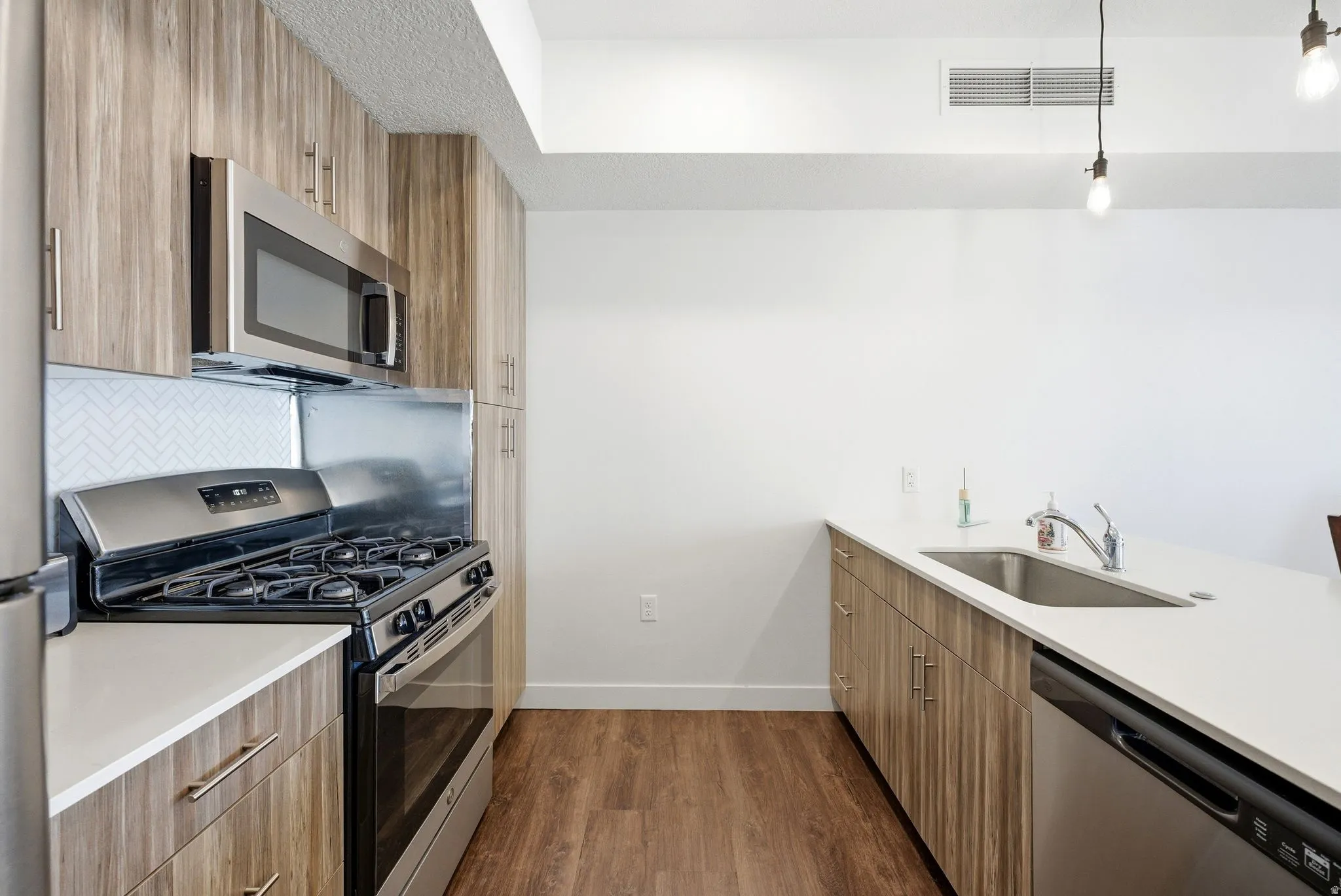 Kitchen featuring stainless steel appliances, modern cabinets, dark wood finished floors, light stone counters, and brown cabinets