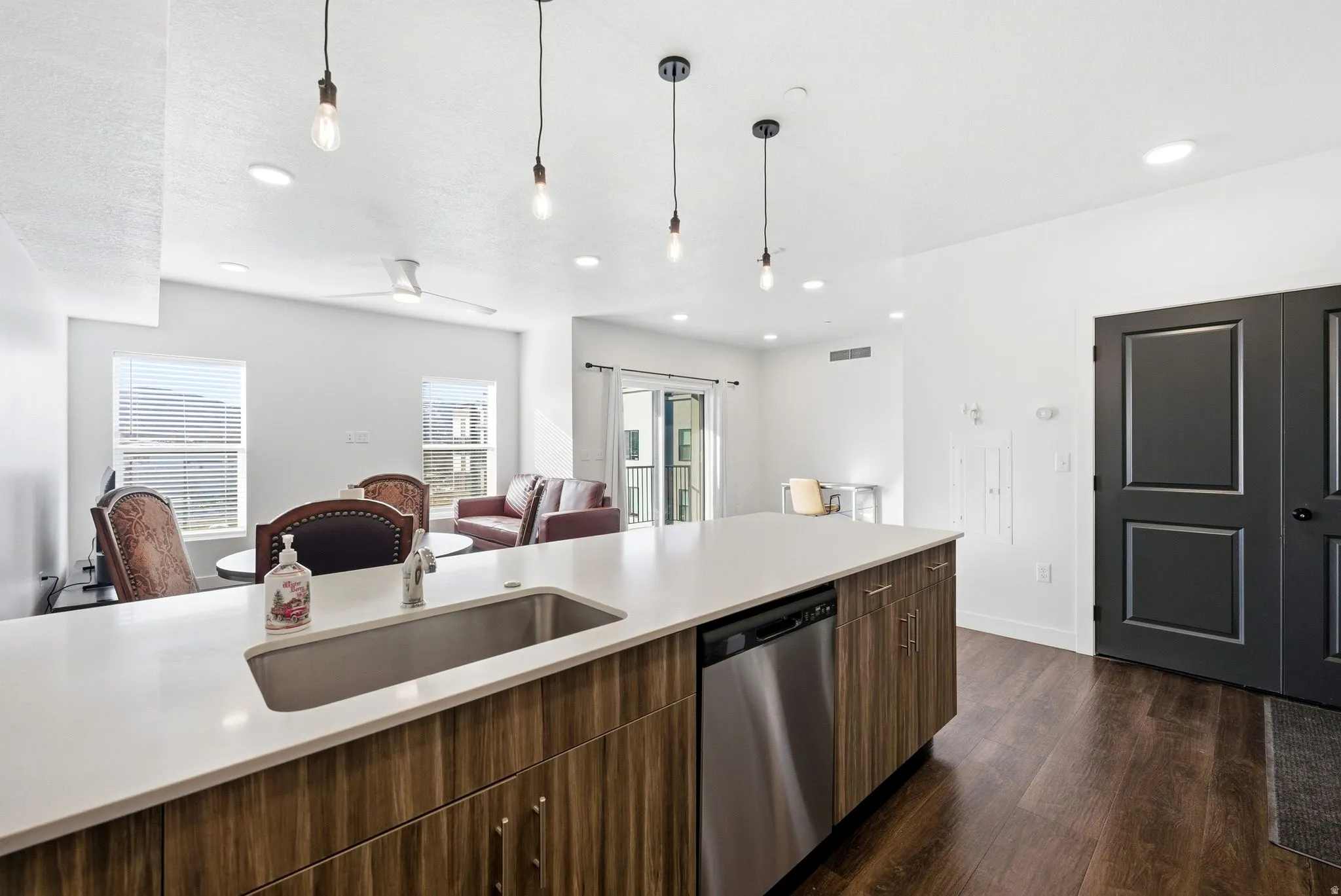Kitchen featuring open floor plan, stainless steel dishwasher, decorative light fixtures, dark wood-style flooring, and dark brown cabinets