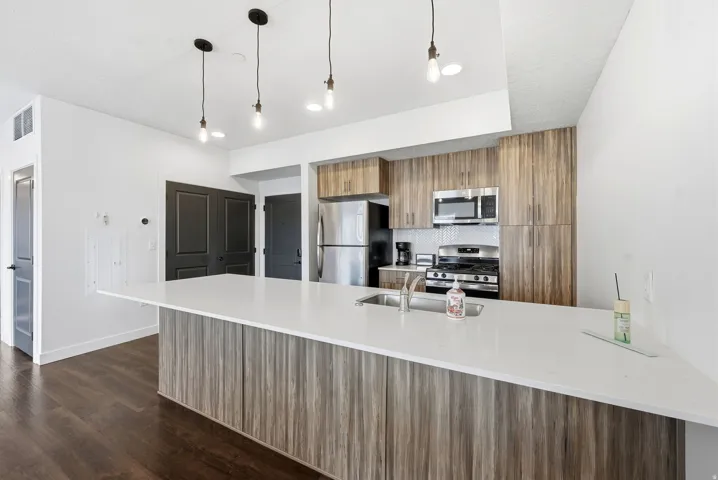 Kitchen featuring modern cabinets, a peninsula, brown cabinets, hanging light fixtures, and stainless steel appliances