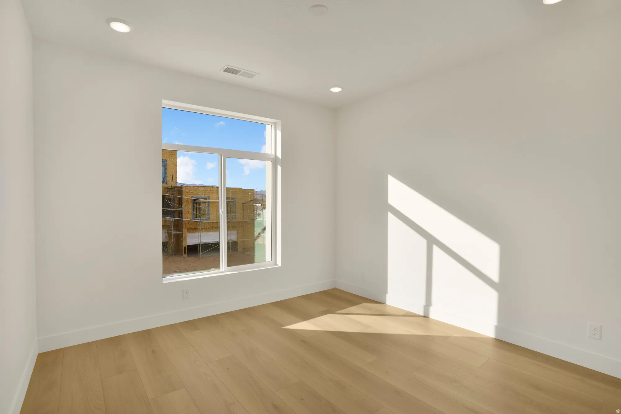 Bright room featuring a large window, recessed lighting, white walls, and wood-finish flooring