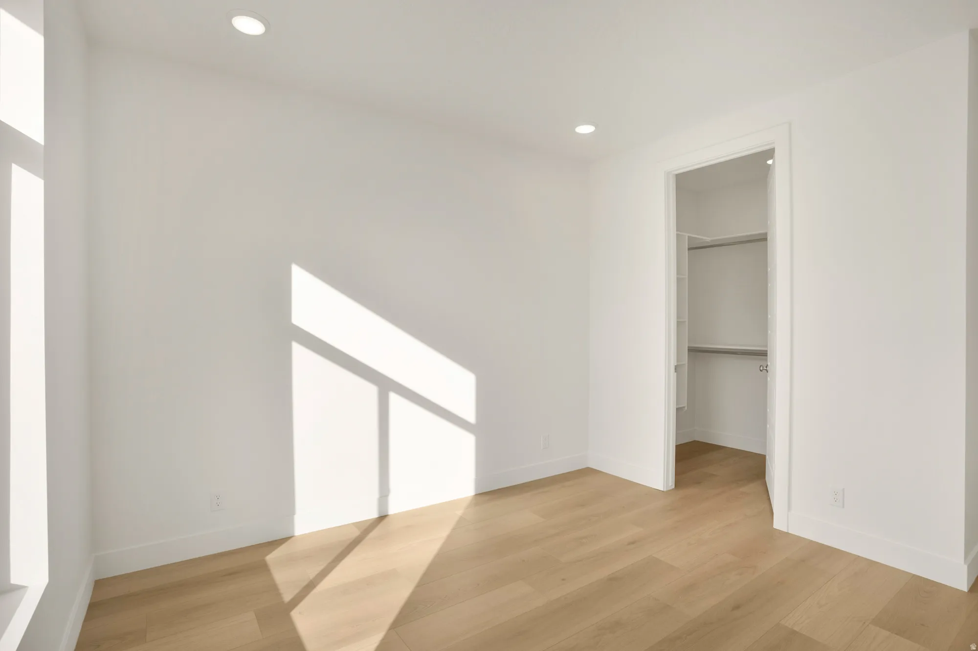 Bright interior space featuring wood-finish flooring, recessed ceiling lighting, a tall window, and a walk-in closet with built-in shelving and hanging rods