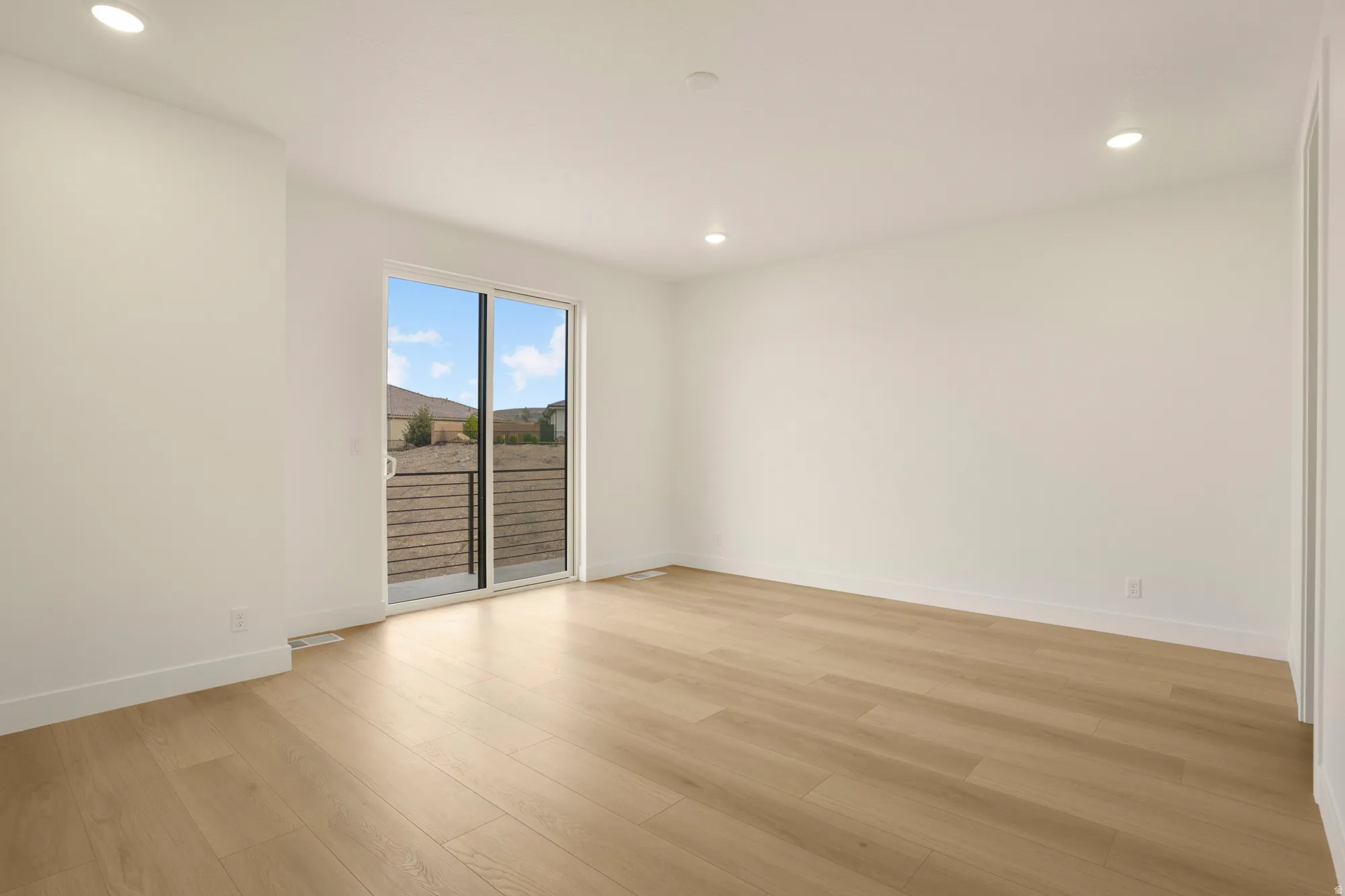 Spacious room featuring light wood-finish flooring and recessed ceiling lighting