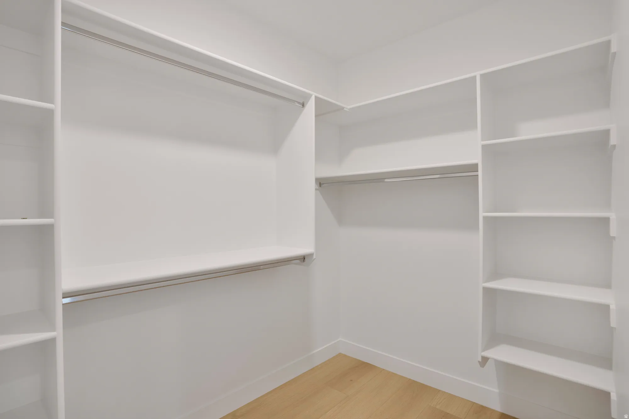 Walk-in closet featuring light wood-finish flooring, white built-in shelving, white walls, and chrome hanging rods