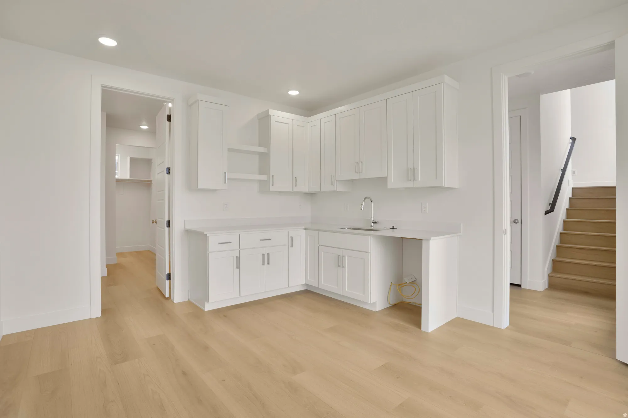 White cabinetry with brushed nickel hardware, light-toned wood-finish flooring, recessed lighting, and a built-in sink with a gooseneck faucet