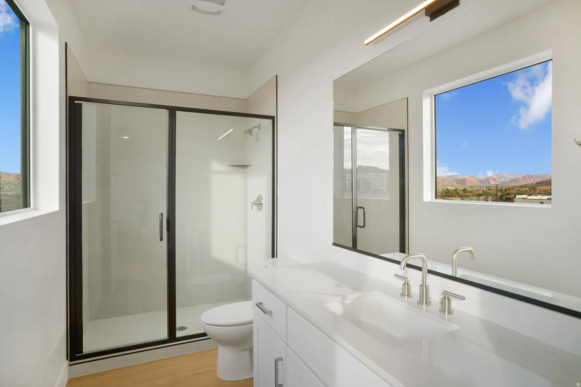 Contemporary bathroom featuring a spacious glass-enclosed shower with black trim, a large vanity with an integrated sink, and an expansive mirror