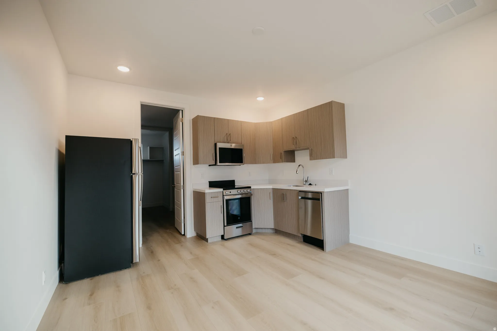 Kitchen with stainless steel appliances, modern cabinets, light wood finished floors, recessed lighting, and light brown cabinets