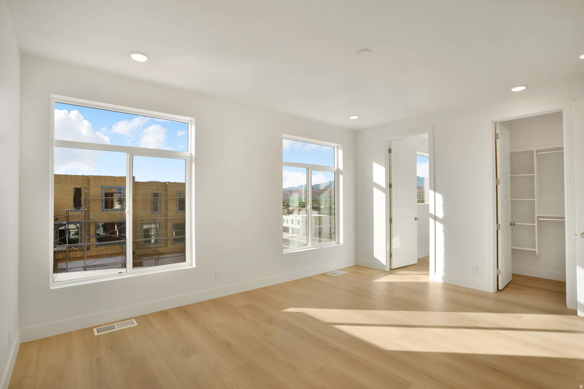 Spacious room featuring multiple large windows, wood-finish flooring, recessed lighting, and a built-in closet system