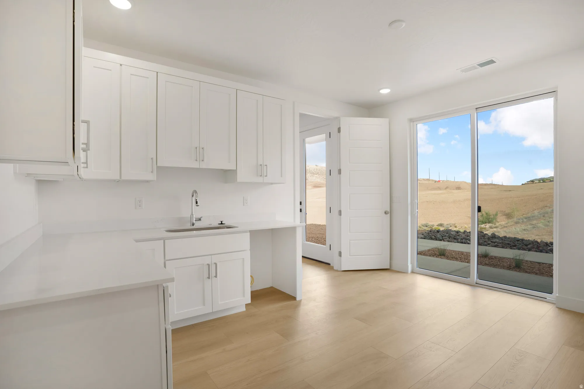 Contemporary space featuring wood-finish flooring, white cabinetry, a stainless steel sink with a gooseneck faucet, and white countertops