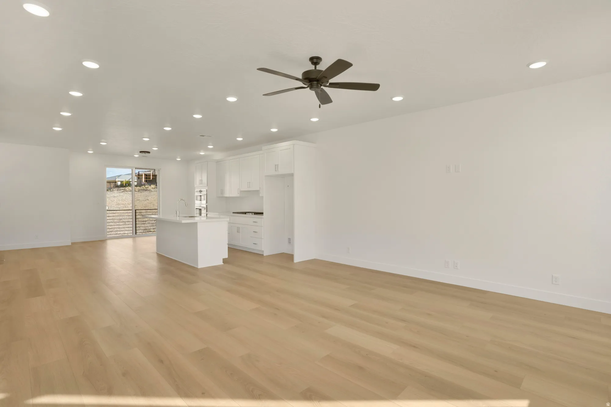 Spacious open-concept area featuring light wood-finish flooring, recessed lighting, and a ceiling fan