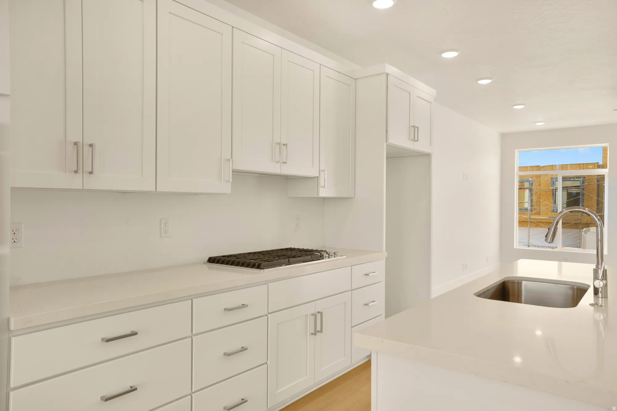 Bright kitchen featuring white shaker cabinetry, light countertops, recessed lighting, a gas cooktop, and a stainless steel sink with a gooseneck faucet