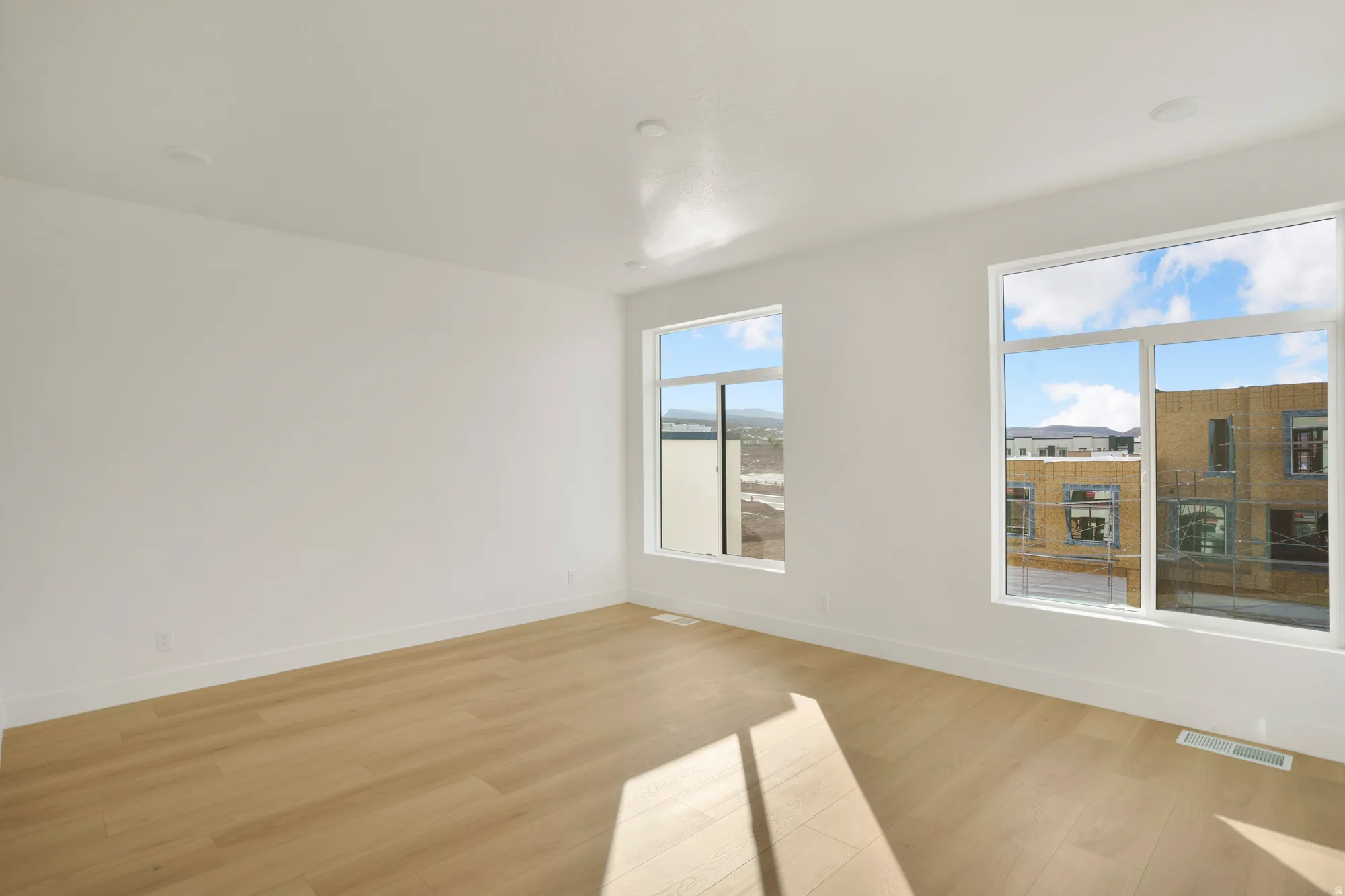 Spacious room featuring light wood-finish flooring, white baseboards, and crisp white walls