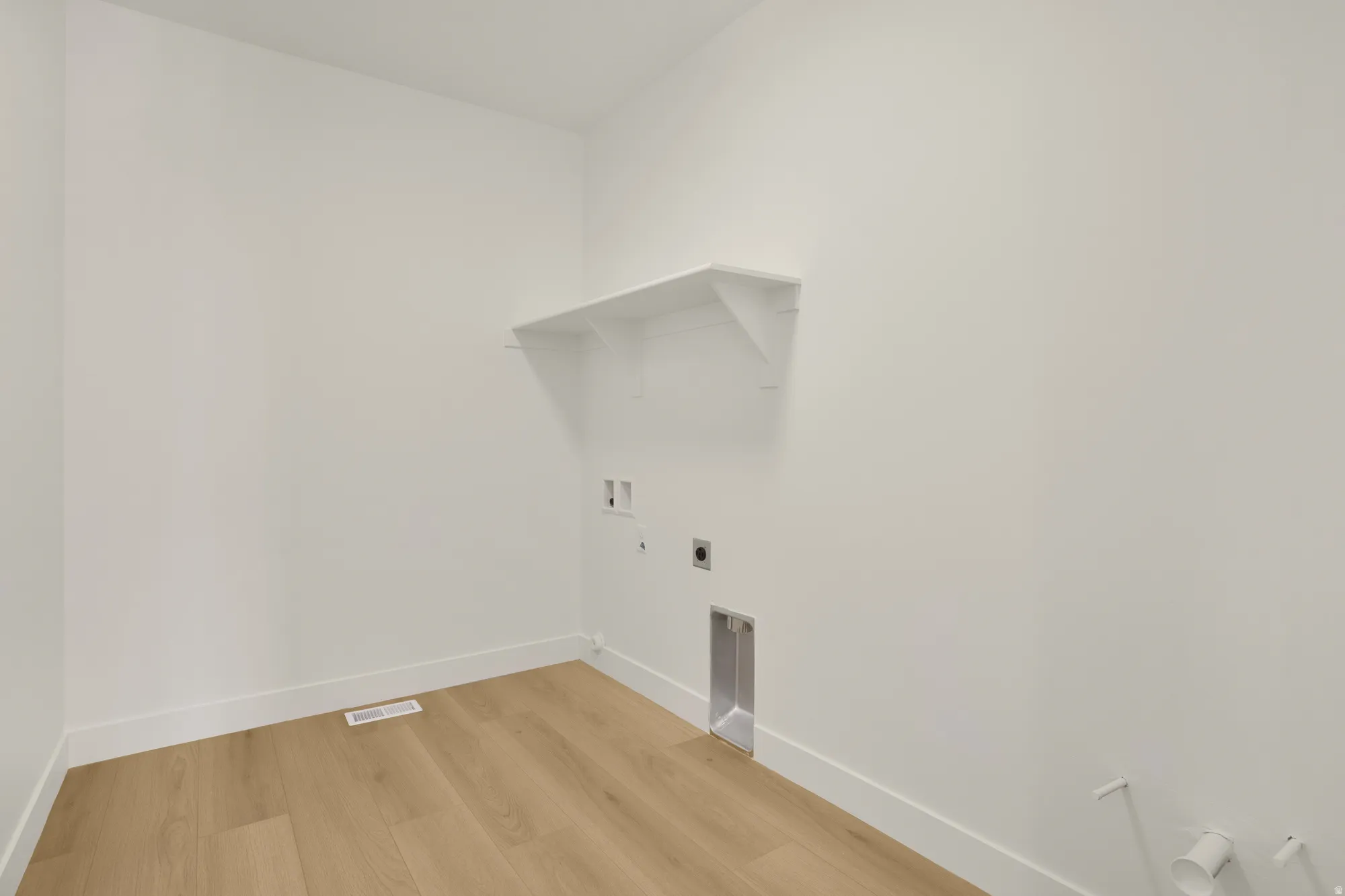 Dedicated laundry space featuring a floating shelf, wood-finish flooring, white walls, and white baseboards