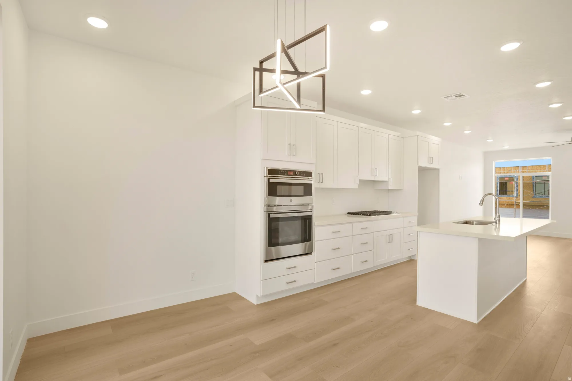Contemporary kitchen featuring white cabinetry, stainless steel double oven, gas cooktop, white countertops, and a central island with an integrated sink