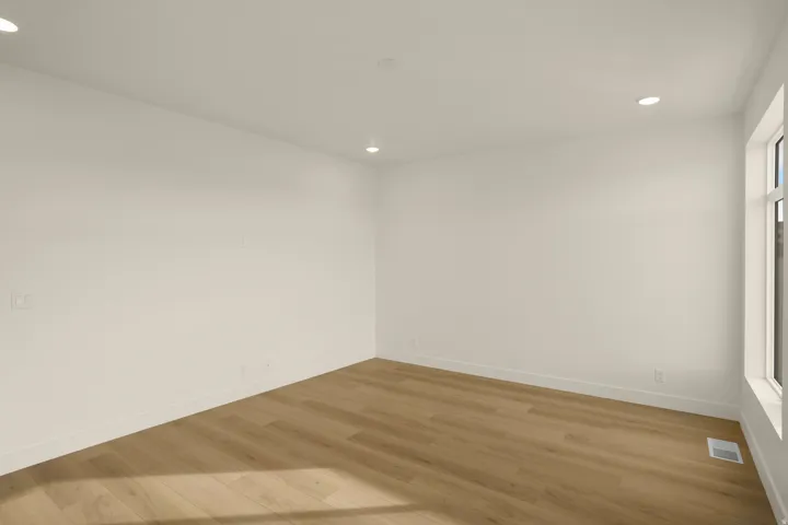Spacious interior room featuring light wood-finish flooring, recessed lighting, white baseboards, and a large window providing ample natural light
