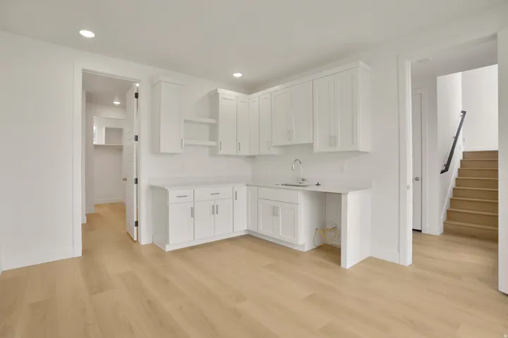 White cabinetry with brushed nickel hardware, light-toned wood-finish flooring, recessed lighting, and a built-in sink with a gooseneck faucet