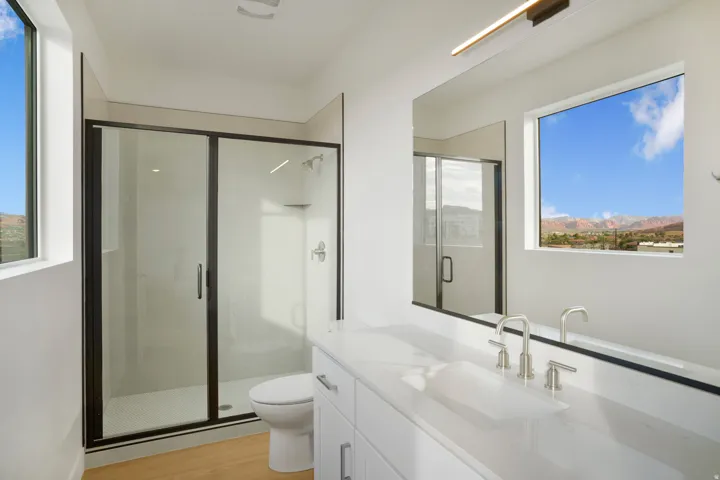 Contemporary bathroom featuring a spacious glass-enclosed shower with black trim, a large vanity with an integrated sink, and an expansive mirror