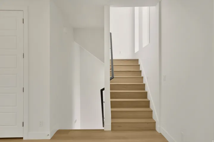 Staircase featuring wood-finish treads and risers, a contemporary black metal railing, crisp white walls, and wood-finish flooring