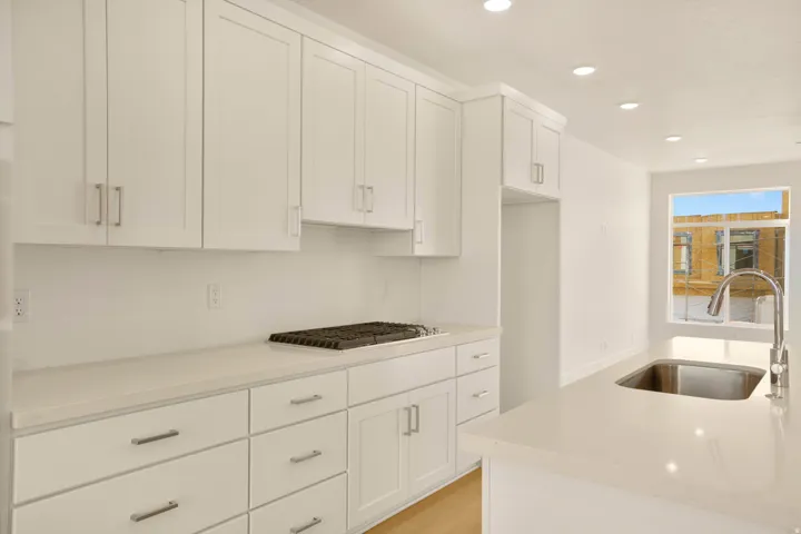 Bright kitchen featuring white shaker cabinetry, light countertops, recessed lighting, a gas cooktop, and a stainless steel sink with a gooseneck faucet
