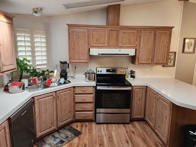 Kitchen featuring appliances with stainless steel finishes, light countertops, lofted ceiling, light wood finished floors, and exhaust hood