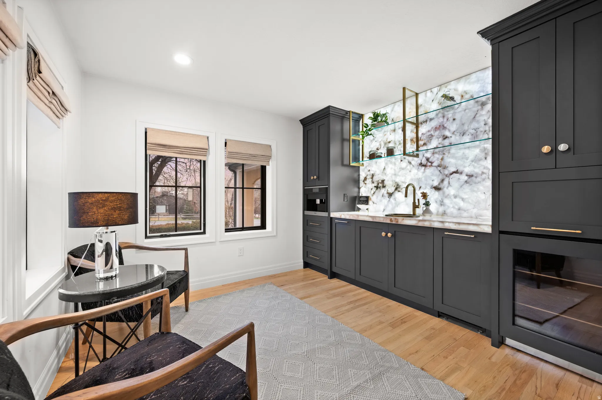 Indoor wet bar featuring light wood finished floors, light stone countertops, recessed lighting, and dark cabinetry