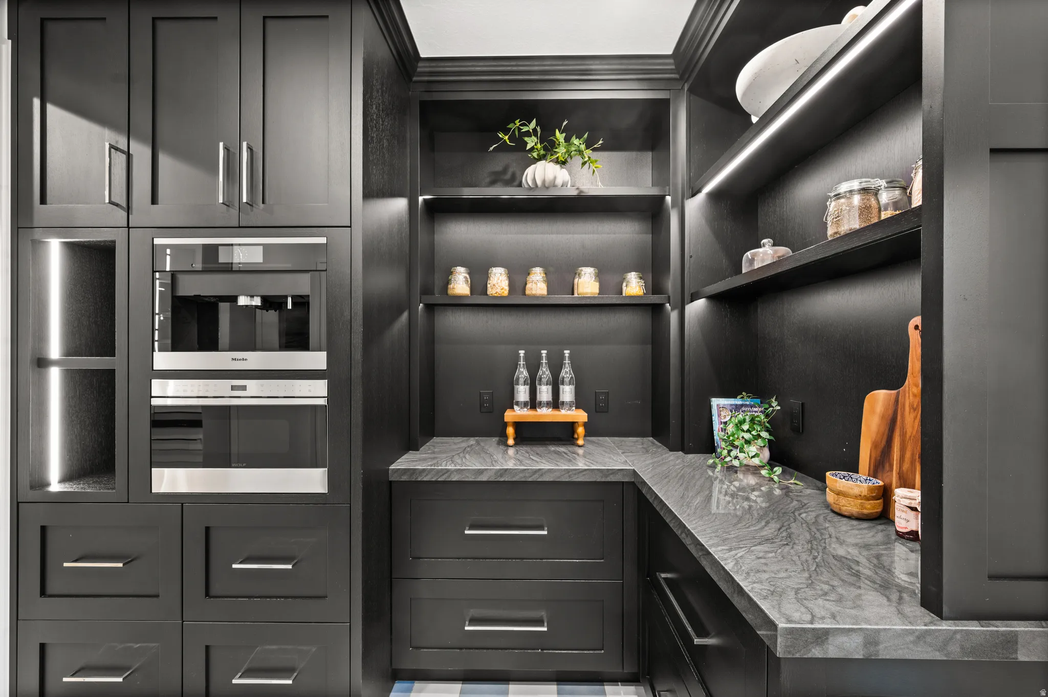 Bar area with open shelves, dark cabinetry, light countertops, crown molding.
