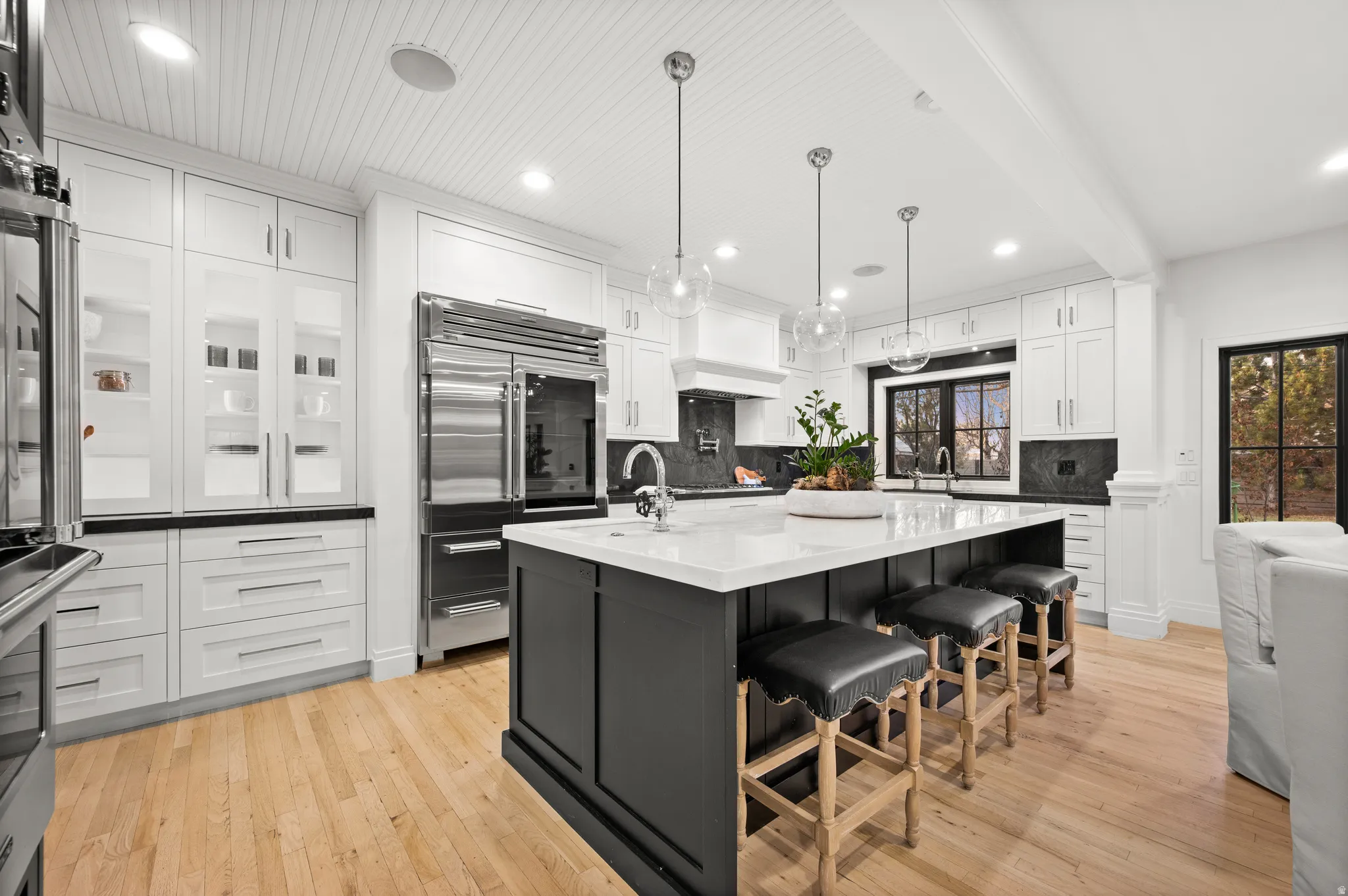 Kitchen with a kitchen bar, stainless steel appliances, light wood-style floors, dark cabinets, and white cabinetry
