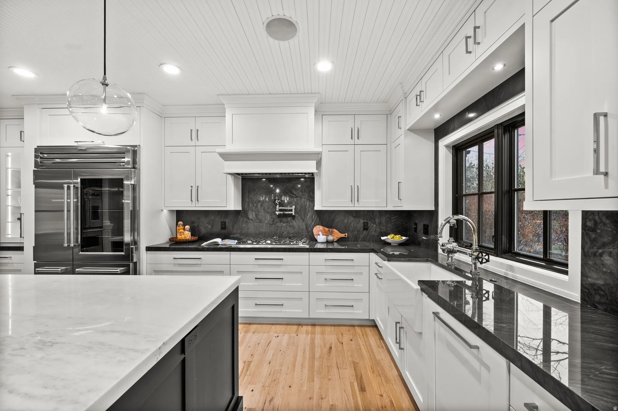 Kitchen with dark stone countertops, light wood-style flooring, dark cabinetry, tasteful backsplash, and stainless steel built in refrigerator