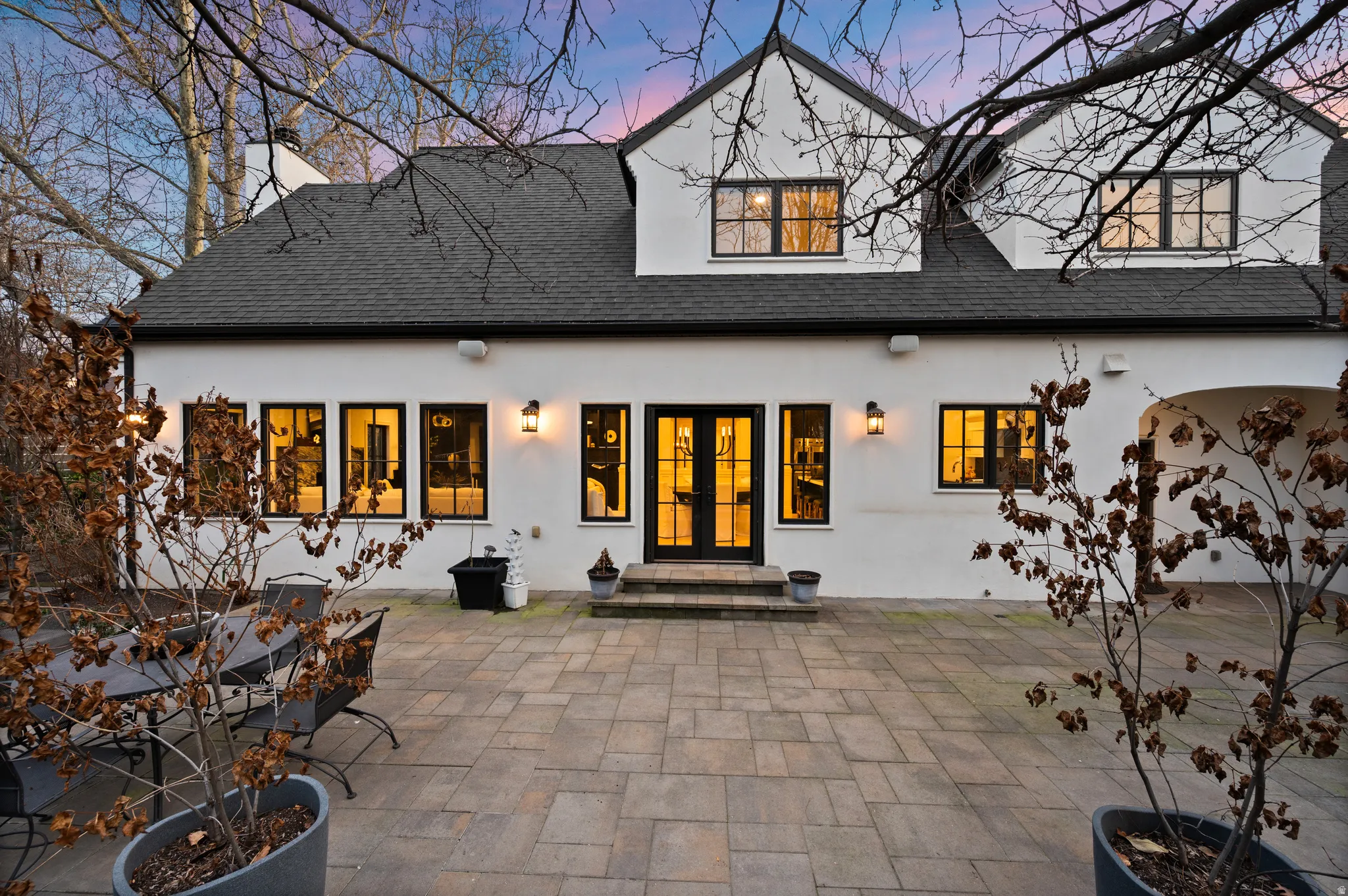 Back of property at dusk with a patio area, french doors, a shingled roof, and stucco siding