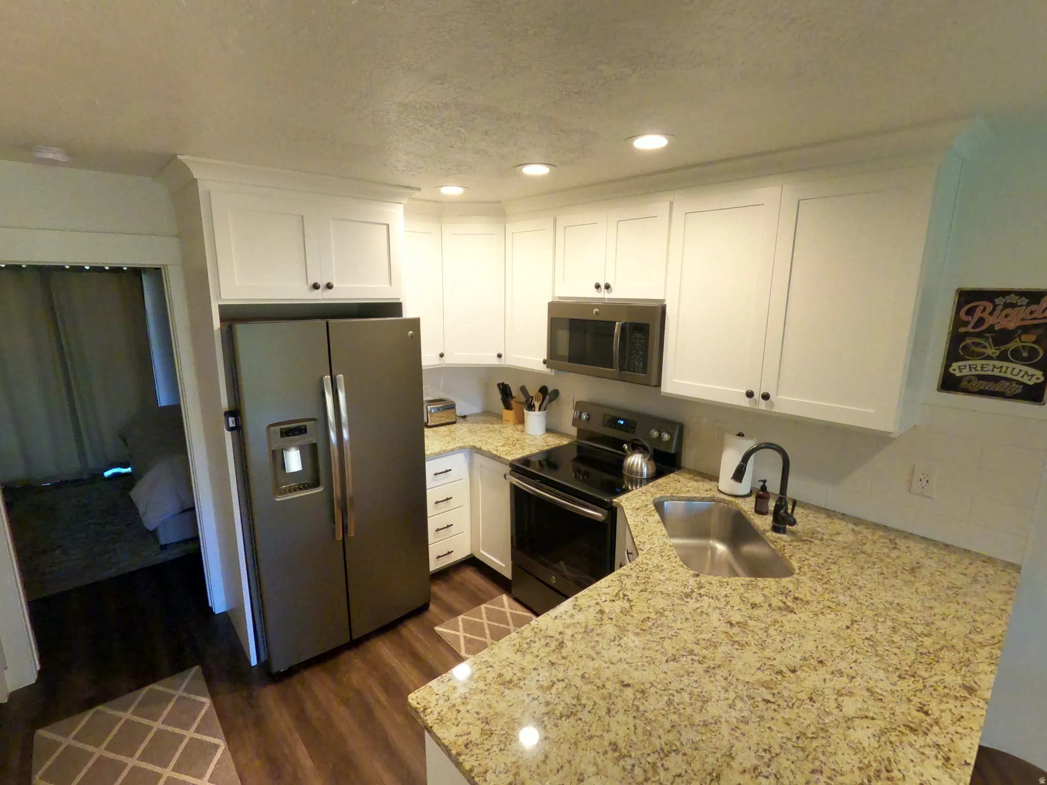 Kitchen with white cabinetry, appliances with stainless steel finishes, light stone countertops, a peninsula, and recessed lighting