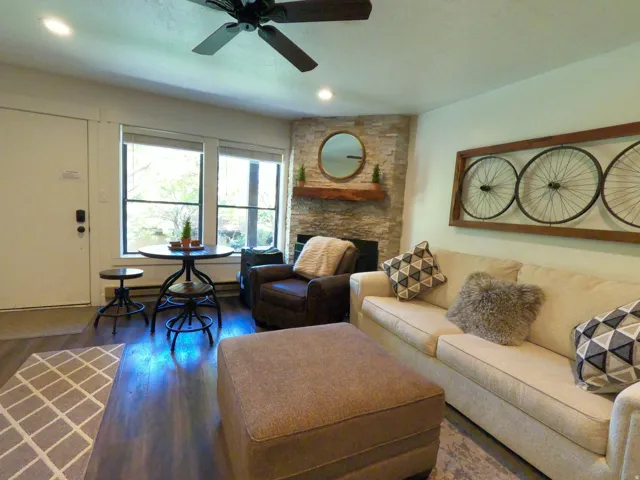 Living room with wood finished floors, a stone fireplace, ceiling fan, and recessed lighting