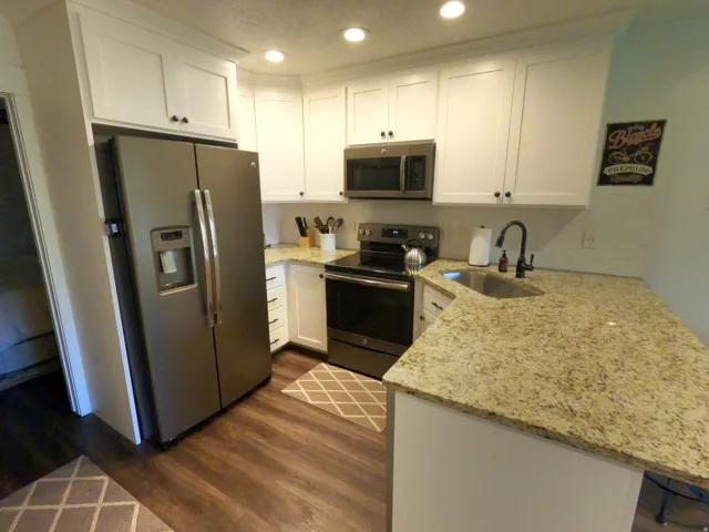 Kitchen featuring stainless steel appliances, white cabinets, light stone countertops, a peninsula, and recessed lighting