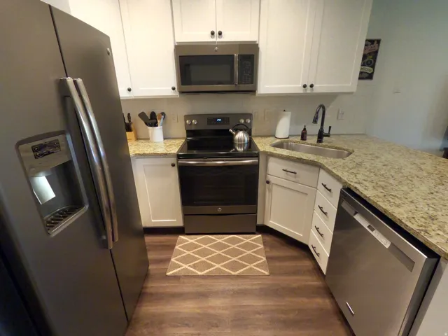 Kitchen with stainless steel appliances, white cabinets, light stone countertops, and decorative backsplash