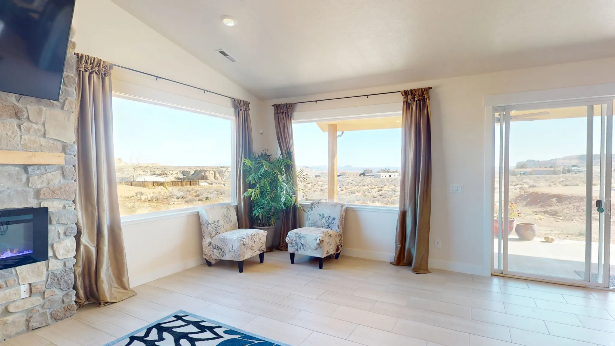 Sitting room with vaulted ceiling, a stone fireplace, and light wood-style floors