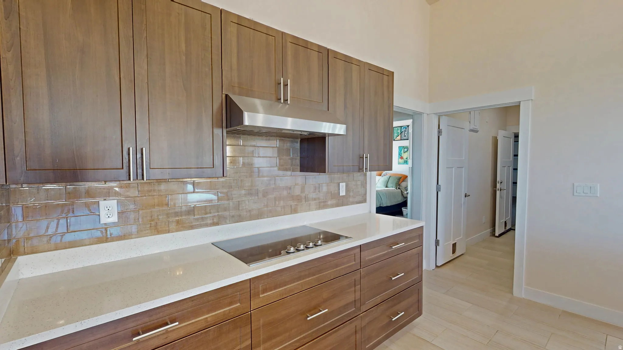 Kitchen featuring brown cabinetry, tasteful backsplash, light stone countertops, under cabinet range hood, and a high ceiling