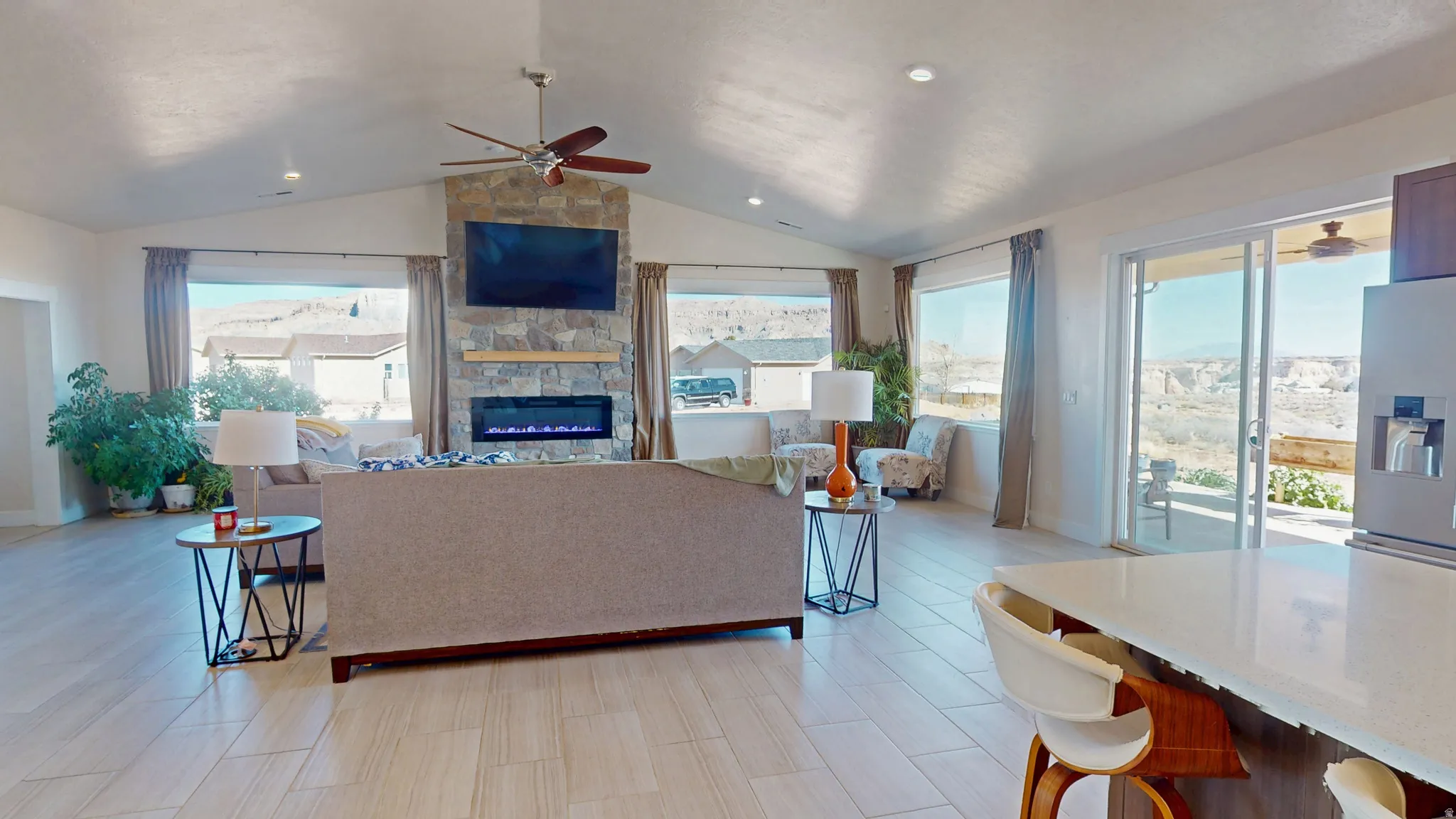 Living area with ceiling fan, wood tiled floors, a stone fireplace, and vaulted ceiling