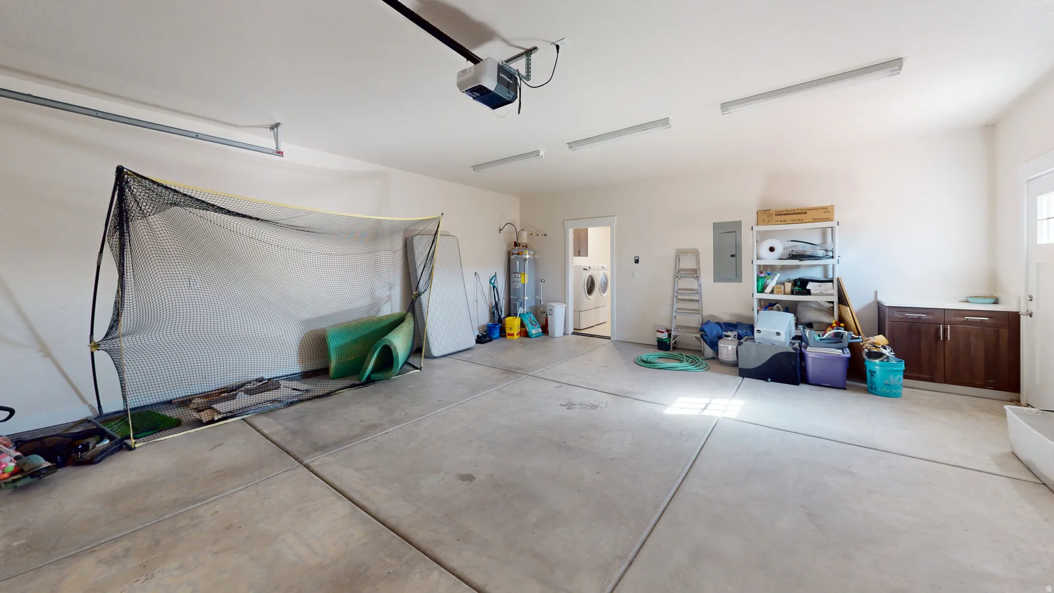 Garage featuring washer and clothes dryer, electric panel, secured water heater, and a garage door opener