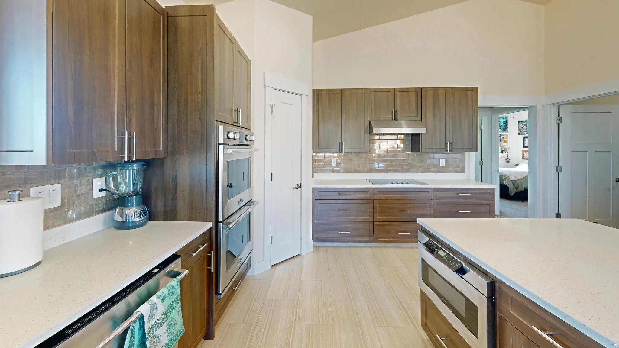Kitchen featuring light stone counters, backsplash, brown cabinets, stainless steel appliances, and high vaulted ceiling