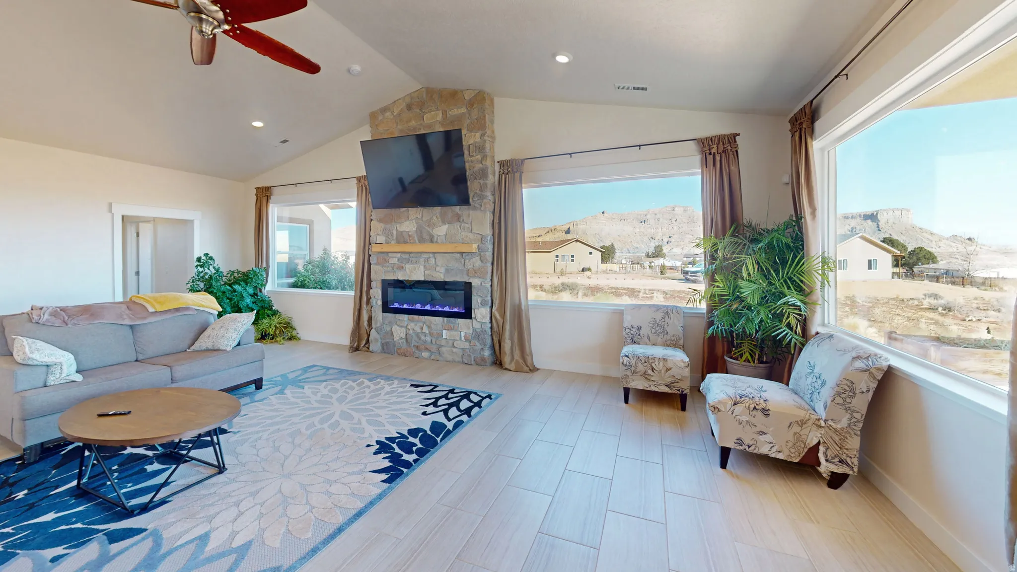 Living room with lofted ceiling, a ceiling fan, a stone fireplace, and wood finished floors